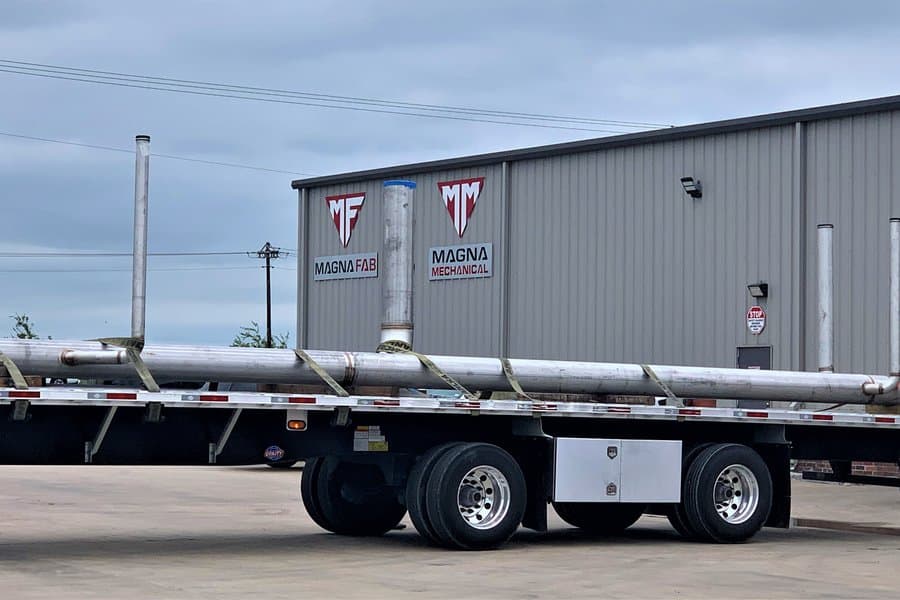 Prefabricated 304 stainless steel drain piping strapped to a flatbed trailer outside the Magna Mechanical fabrication facility